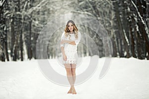 Beautiful young woman in a light dress and barefoot in the snow