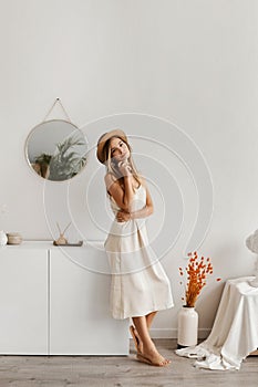 Beautiful young woman in a light dress and hat posing in the interior. Model girl in summer outfit and with a big bag in