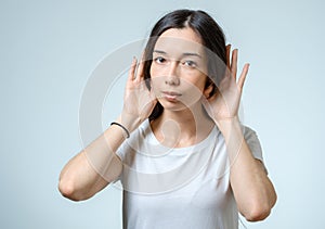 Beautiful young woman listening gossips and holding her hand near the ear