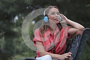 Beautiful young woman listening musing through headphones in park