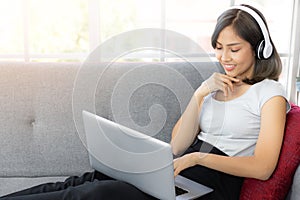 Beautiful young woman listening to music in headphones and keeping eyes closed while sitting on sofa