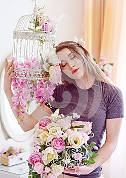 Beautiful young woman with long blonde hair, blue eyes, flowering cage, wearing t-shirt.