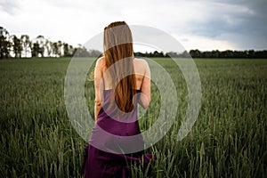 Beautiful young woman with long blonde hair in motion turned back, on the green field.Summer and freedom concept.