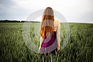 Beautiful young woman with long blonde hair in motion turned back, on the green field.Summer and freedom concept.