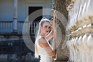 Beautiful young woman with long blonde hair and a short white dress leaning against a wall. The woman is sad and depressed.