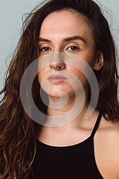 beautiful young woman with long brown curly hair in the studio. A girl with a nose piercing looks at the camera.