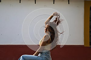 Beautiful young woman with long curly hair against a white and red background. The woman is sitting on a stool in the street. The