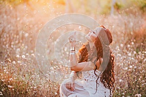 Beautiful young woman with long curly hair dressed in boho style dress posing in a field with dandelions