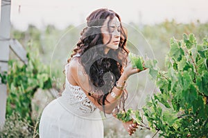 Beautiful young woman with long curly hair dressed in boho style dress posing in a field with dandelions
