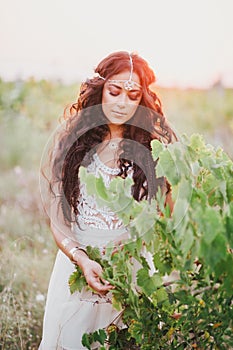 Beautiful young woman with long curly hair dressed in boho style dress posing in a field with dandelions