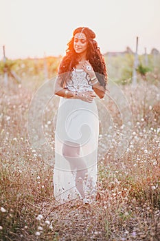 Beautiful young woman with long curly hair dressed in boho style dress posing in a field with dandelions