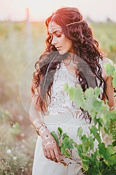 Beautiful young woman with long curly hair dressed in boho style dress posing in a field with dandelions