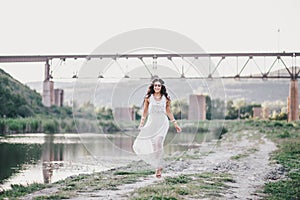 Beautiful young woman with long curly hair dressed in boho style dress posing near lake
