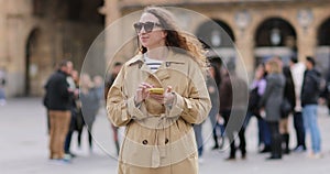 beautiful young woman with long curly hair is wearing sunglasses and using cellphone. girl out and about in the city