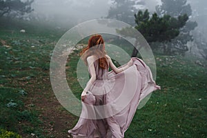 Beautiful young woman in a long dress in the mountains by the forest