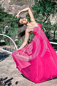 Beautiful young woman in a long evening dress posing in nature, developing it