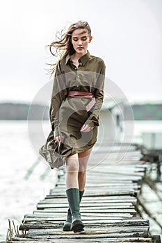 Beautiful young woman in long green dress on wooden panton by the river photo