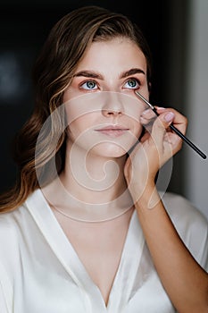 A beautiful young woman with long hair doing makeup for a wedding or photo shoot