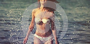Beautiful young woman with long hair runs along sea beach, splashes of water. Happiness, joy, vacation, travel concept