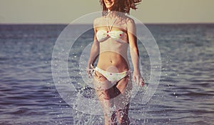 Beautiful young woman with long hair runs along sea beach, splashes of water. Happiness, joy, vacation, travel concept