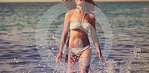 Beautiful young woman with long hair runs along sea beach, splashes of water. Happiness, joy, vacation, travel concept