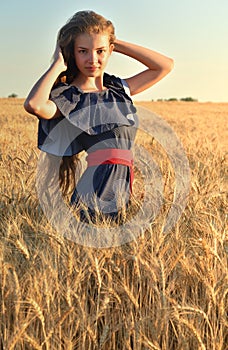 A beautiful young woman with long hair standing in the wheat field. Touches her hair