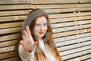 Beautiful young woman with long hair stretches her hand forward to camera, Caucasian woman sitting on a wooden bench and pulling