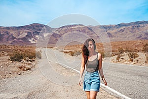 Beautiful young woman with long hair walks along a picturesque empty road in Death Valley overlooking the mountains, USA