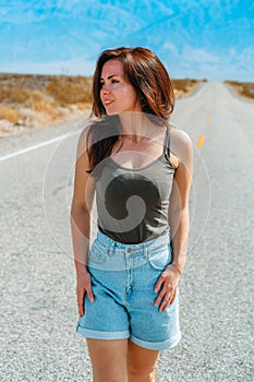 Beautiful young woman with long hair walks along a picturesque empty road in Death Valley overlooking the mountains, USA