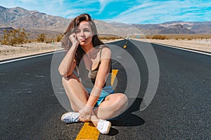 Beautiful young woman with long hair walks along a picturesque empty road in Death Valley overlooking the mountains, USA