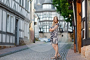 Beautiful young woman with long hairs in summer dress going for a walk in German city. Happy girl enjoying walking in