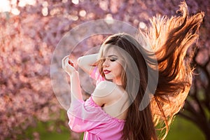 Beautiful young woman with long healthy blowing hair running in blossom park at sunset.