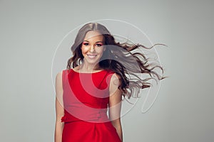 Beautiful young woman with long healthy curly hair and bright make up wearing red dress  on grey studio