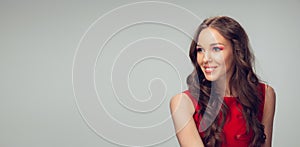 Beautiful young woman with long healthy curly hair and bright make up wearing red dress  on grey studio