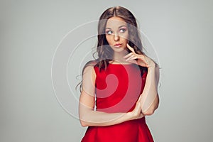 Beautiful young woman with long healthy curly hair and bright make up wearing red dress isolated on grey studio