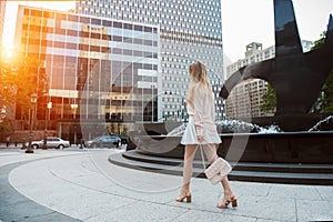 Beautiful young woman with long legs walking on city street wearing short skirt and pink t-shirt and holding a bag