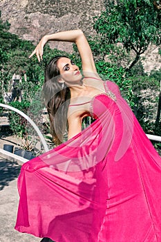 Beautiful young woman in a long pink evening dress posing in nature, developing it
