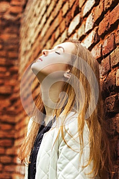 Beautiful young woman with long red hair stands near the red wall street in the city