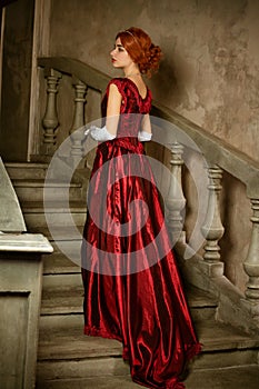 A beautiful young woman in a long red retro dress is standing on the stairs