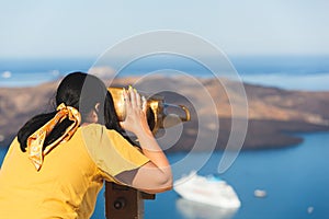 Beautiful woman looking at cruise ships with binoculars in Thira, Santorini, Greece