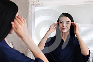 Beautiful young woman looking at herself in bathroom mirror