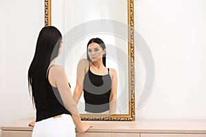 Beautiful young woman looking at herself in mirror