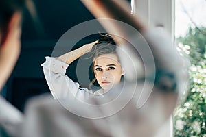 Beautiful young woman looking herself reflection in mirror