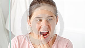 Beautiful young woman looking in the mirror and checking her teeth with finger. Concept of teeth health, self checking mouth and