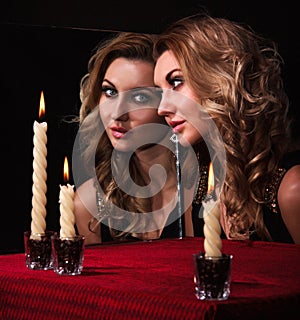 Beautiful young woman looking in the mirror near three candles
