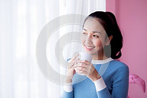 Beautiful young woman is looking out the window and holding a cup of coffee.