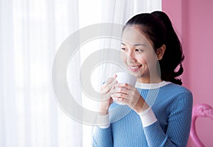 Beautiful young woman is looking out the window and holding a cup of coffee in morning.