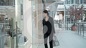 Beautiful young woman looking in a shop window with clothes and dresses and luxury juwellery in shopping mall, business