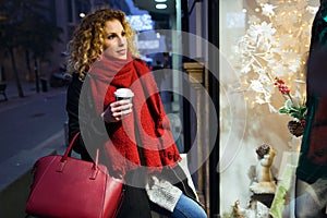 Beautiful young woman looking at the shop window at night.