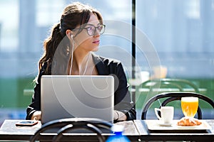 Beautiful young woman looking sideways while working with her laptop in a coffee shop.